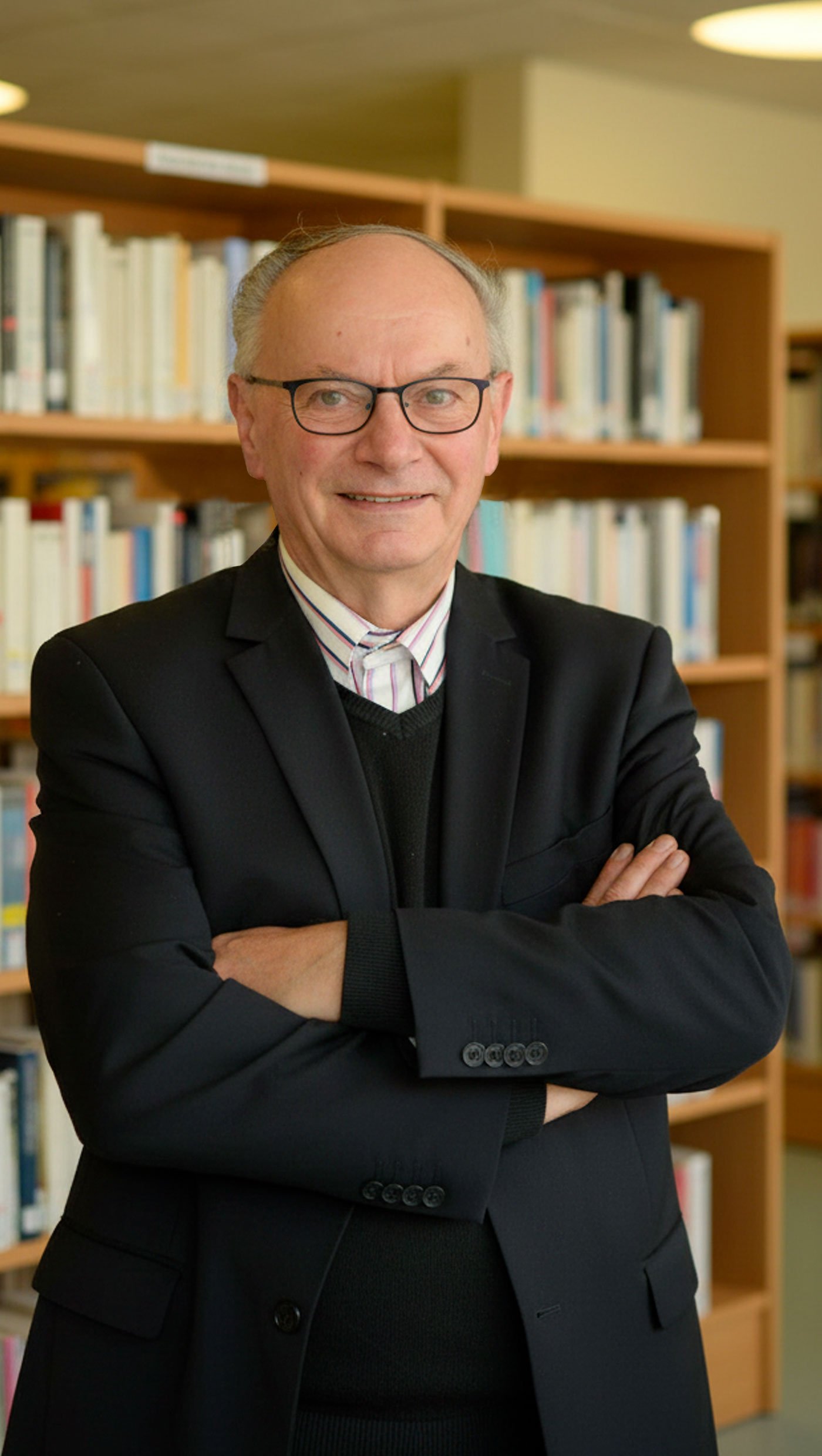 Alain LARCHIER debout devant une bibliothèque