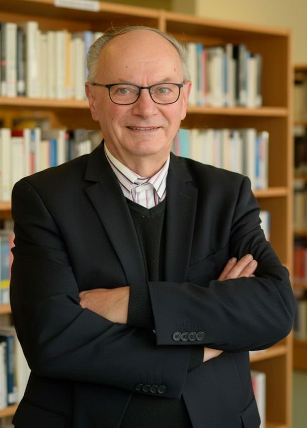 Alain LARCHIER debout devant une bibliothèque